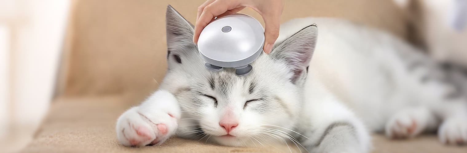 Hand using a cat massager on a cat’s head; handheld device with rotating silicone heads for gentle relief